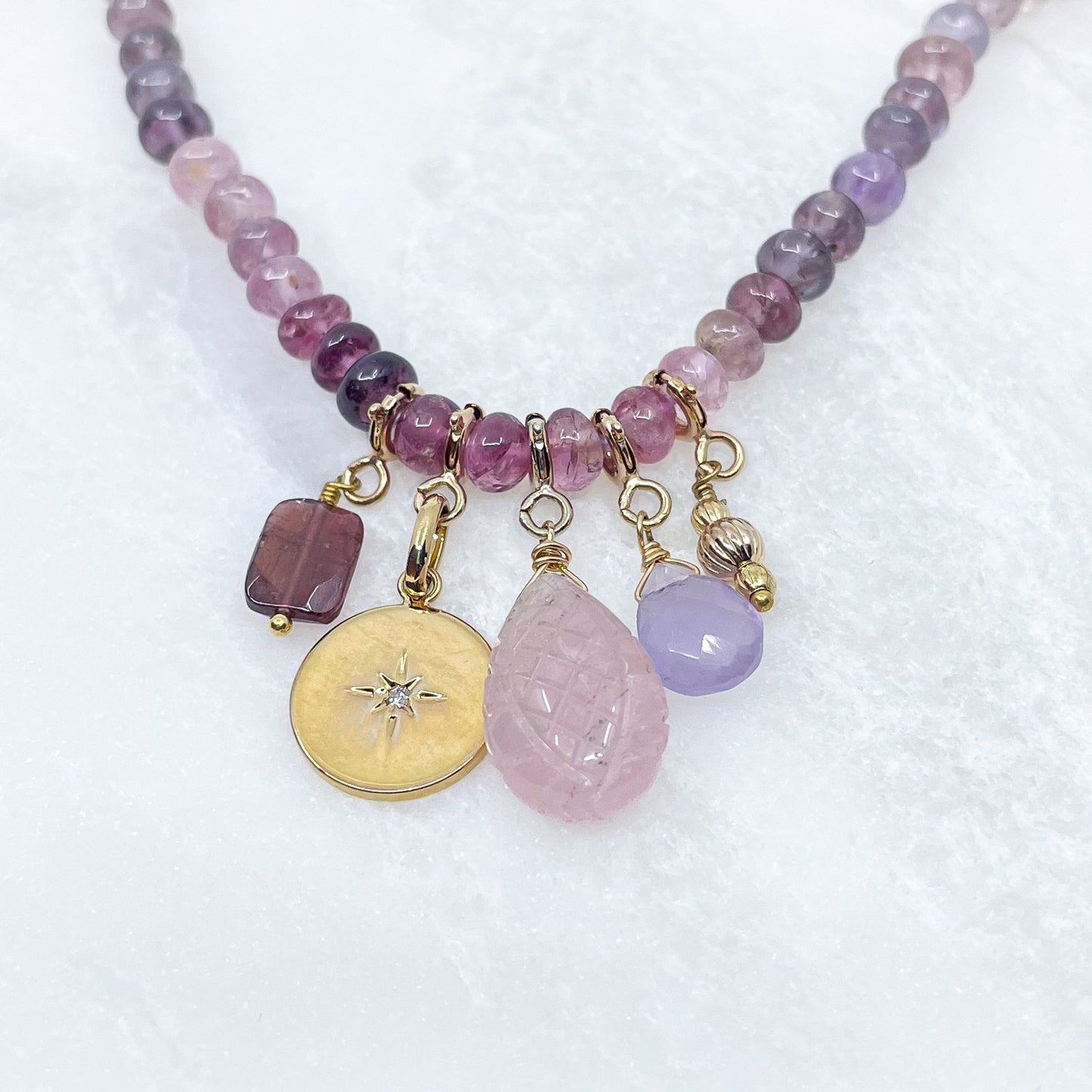 Collier long de 58 cm en pierres fines naturelles de spinelle dans des dégradés de rose à bleu gris. 5 charms : 3 pierres fines naturelles de teintes harmonieuses, une médaille ronde et un pendentif en petites perles plaqué or. Chaîne de réglage de 4 cm et fermoir plaqué or 18 carats