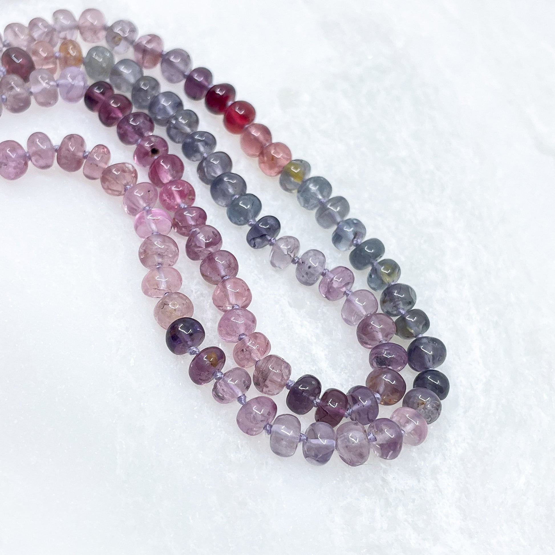 Collier long de 58 cm en pierres fines naturelles de spinelle dans des dégradés de rose à bleu gris. 5 charms : 3 pierres fines naturelles de teintes harmonieuses, une médaille ronde et un pendentif en petites perles plaqué or. Chaîne de réglage de 4 cm et fermoir plaqué or 18 carats