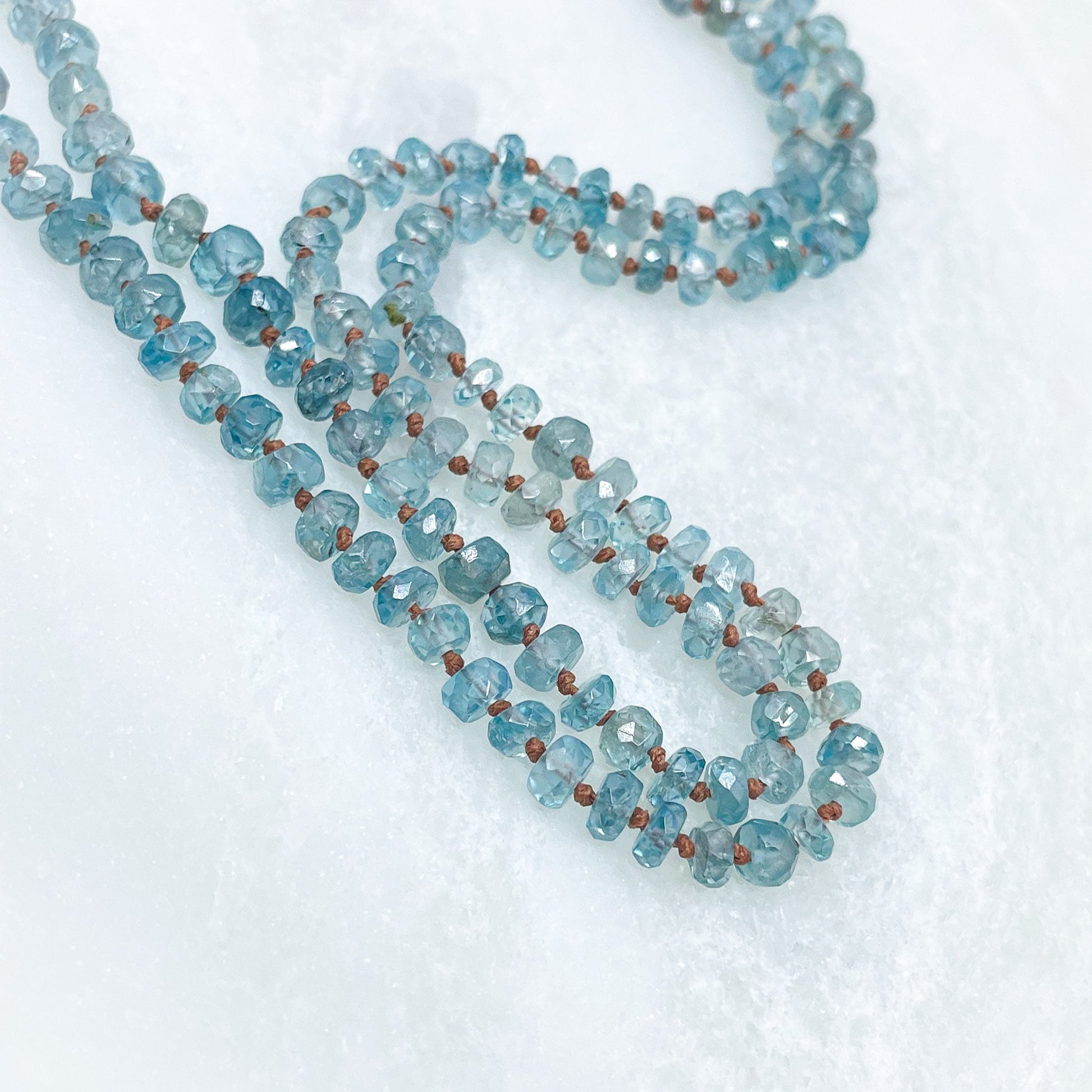 Collier long de 60 cm en pierres fines de zircon naturel d'un bleu azur. 5 charms : 3 pierres fines naturelles de teintes bleu-vert, une médaille ronde et un pendentif en petites perles plaqué or. Chaîne de réglage de 4 cm et fermoir plaqué or 18 carats